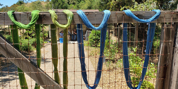 four skeins of blue and green yarn drying on the fence